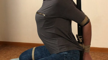 Ring-gagged barefoot Gloria in t-shirt and jeans, tied kneeling to the stick with her elbows tightly bound together, wig.webp