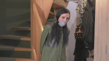 Miss Amira im sexy Lackoutfit und Ilse Jacobsen Regenmantel wird gefesselt und geknebelt.webp