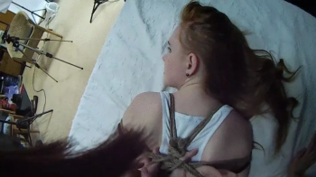 Barefoot Amy in white tank-top and jeans shorts, hogtied with hemp rope, is tickled and teased by Blackshark - view from.webp